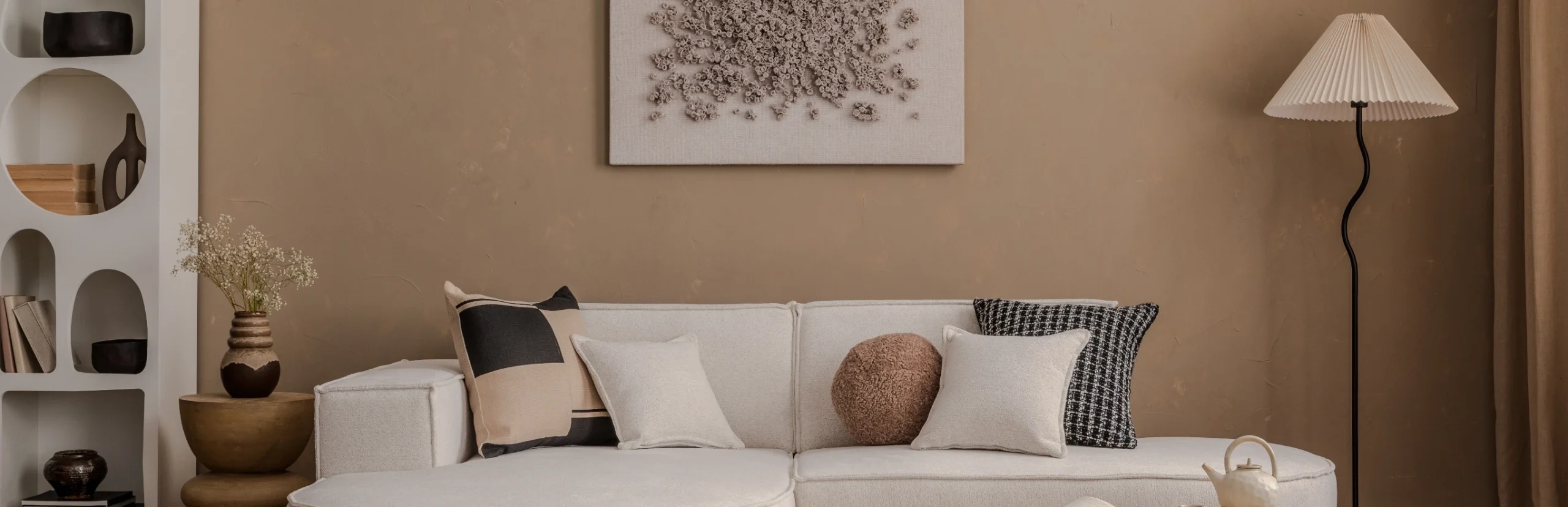 Beige målad vägg med vit soffa, golvlampa och hylla